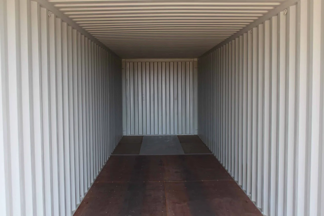 Empty container interior showing bare corrugated steel walls and plywood floor before shelving